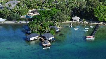 An aerial view of a tropical island with overwater bungalows, clear blue water, and a dock with boats.