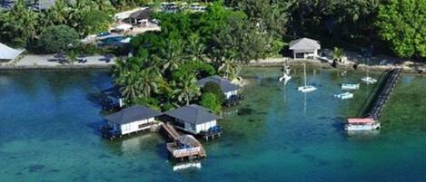 An aerial view of a tropical island with overwater bungalows, clear blue water, and a dock with boats.