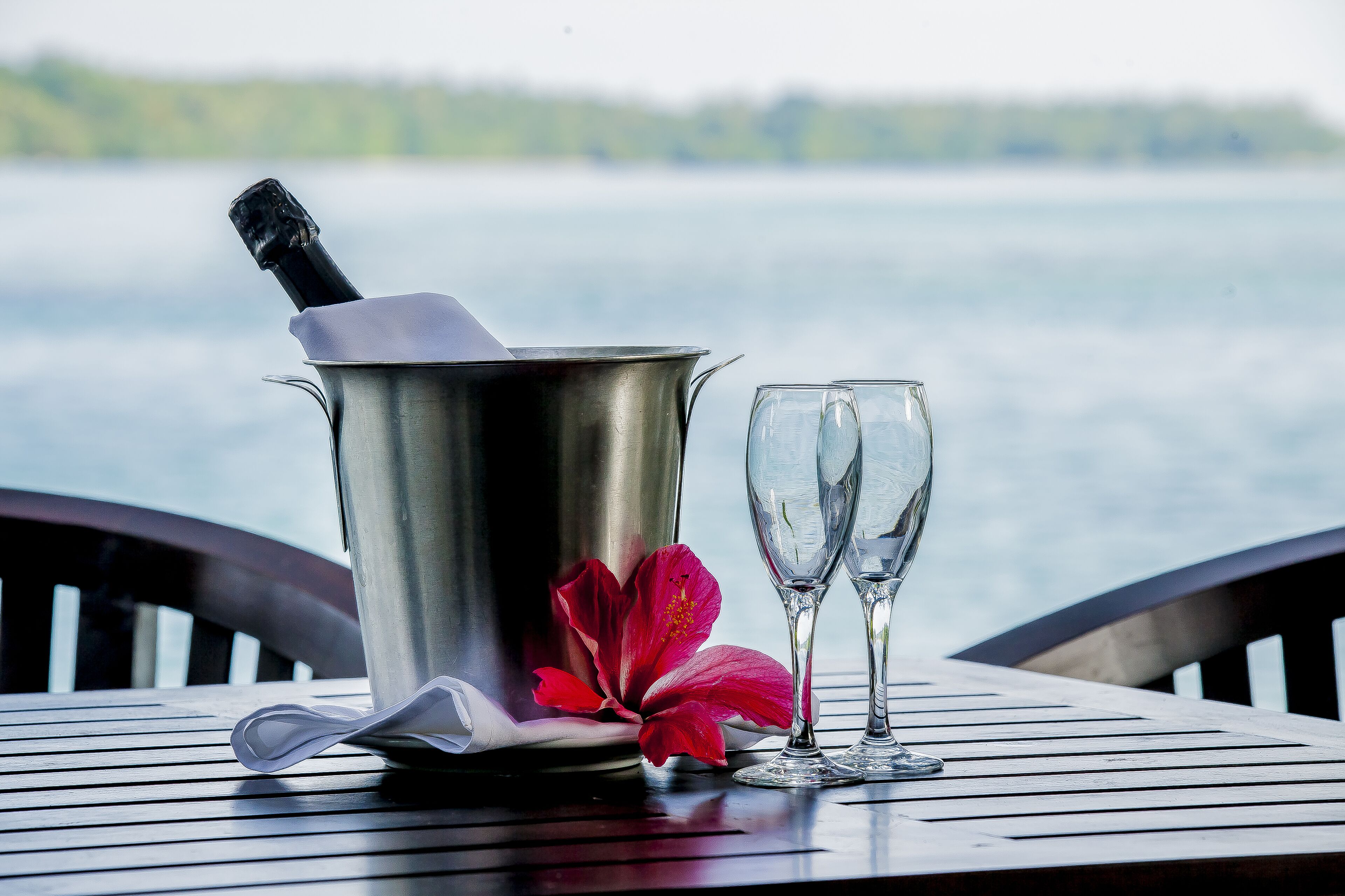Une table avec une bouteille de champagne, deux verres et une fleur rouge.