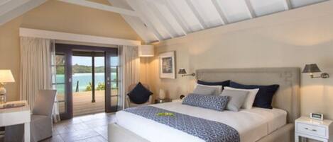 Un dormitorio amplio con una cama grande, un escritorio y una silla. Cuenta con un balcón con vistas al mar.
