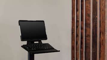 A laptop on a stand with a keyboard, positioned against a plain wall with vertical wooden slats.