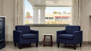 Una habitación con dos sillones azules, una mesita redonda y vistas a un edificio con techo rojo a través de una ventana con cortinas estampadas.
