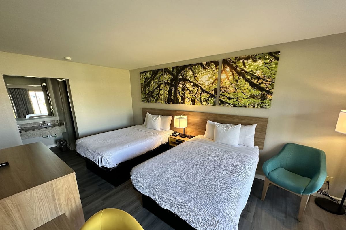 Habitación de hotel con dos camas, un escritorio, una silla, un cuadro y una lámpara.