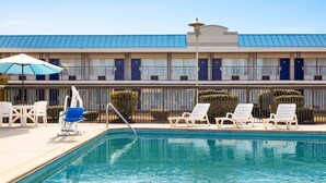 Un hotel con piscina, sillas de descanso y un toldo azul.