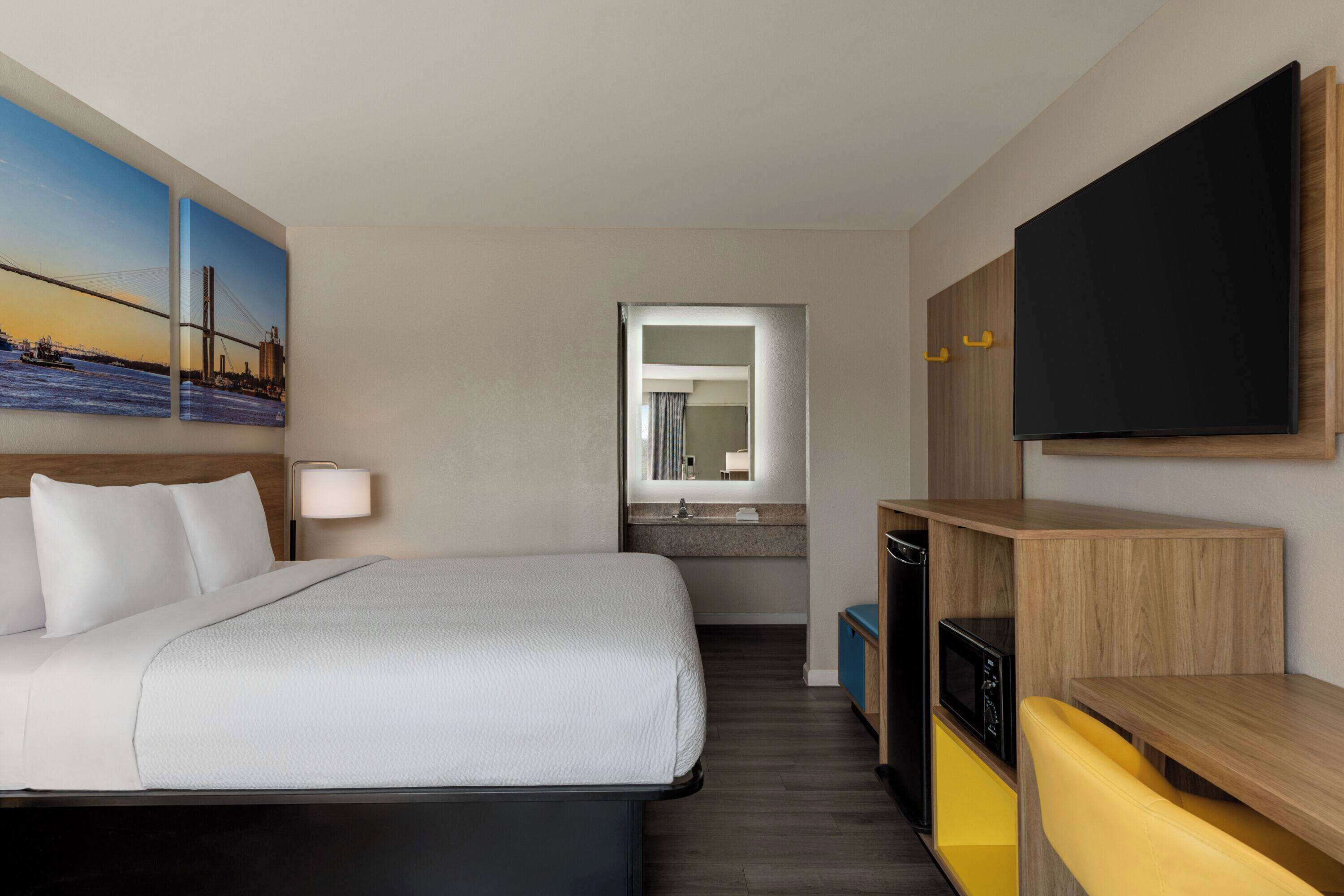 Une chambre d’hôtel avec un lit, une télévision, un bureau et une salle de bain visible à travers une porte ouverte.