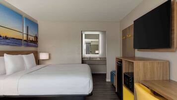 A hotel room with a bed, a TV, a desk, and a bathroom visible through an open door.