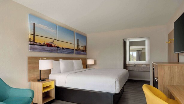 Una habitación de hotel con una cama, un escritorio, una silla, una mesita de noche, una lámpara y un cuadro de un puente.