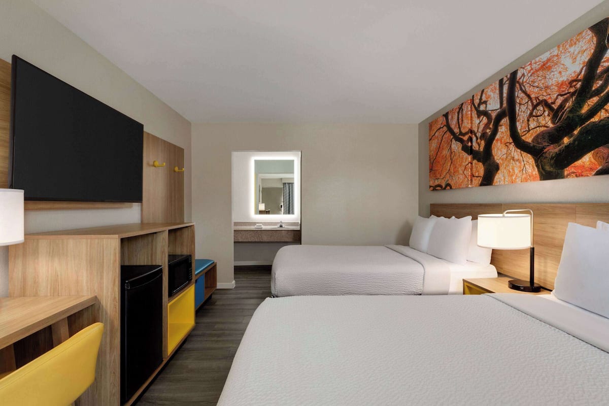 Una habitación de hotel con cama, escritorio, televisor, baño y un cuadro.