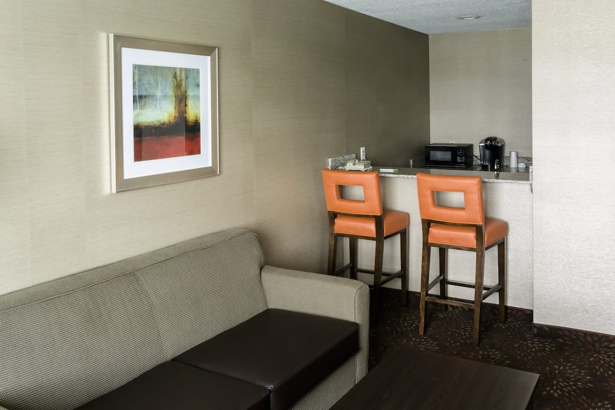 Habitación de hotel con sofá, dos taburetes altos, una pequeña cocina con microondas y un cuadro en la pared.