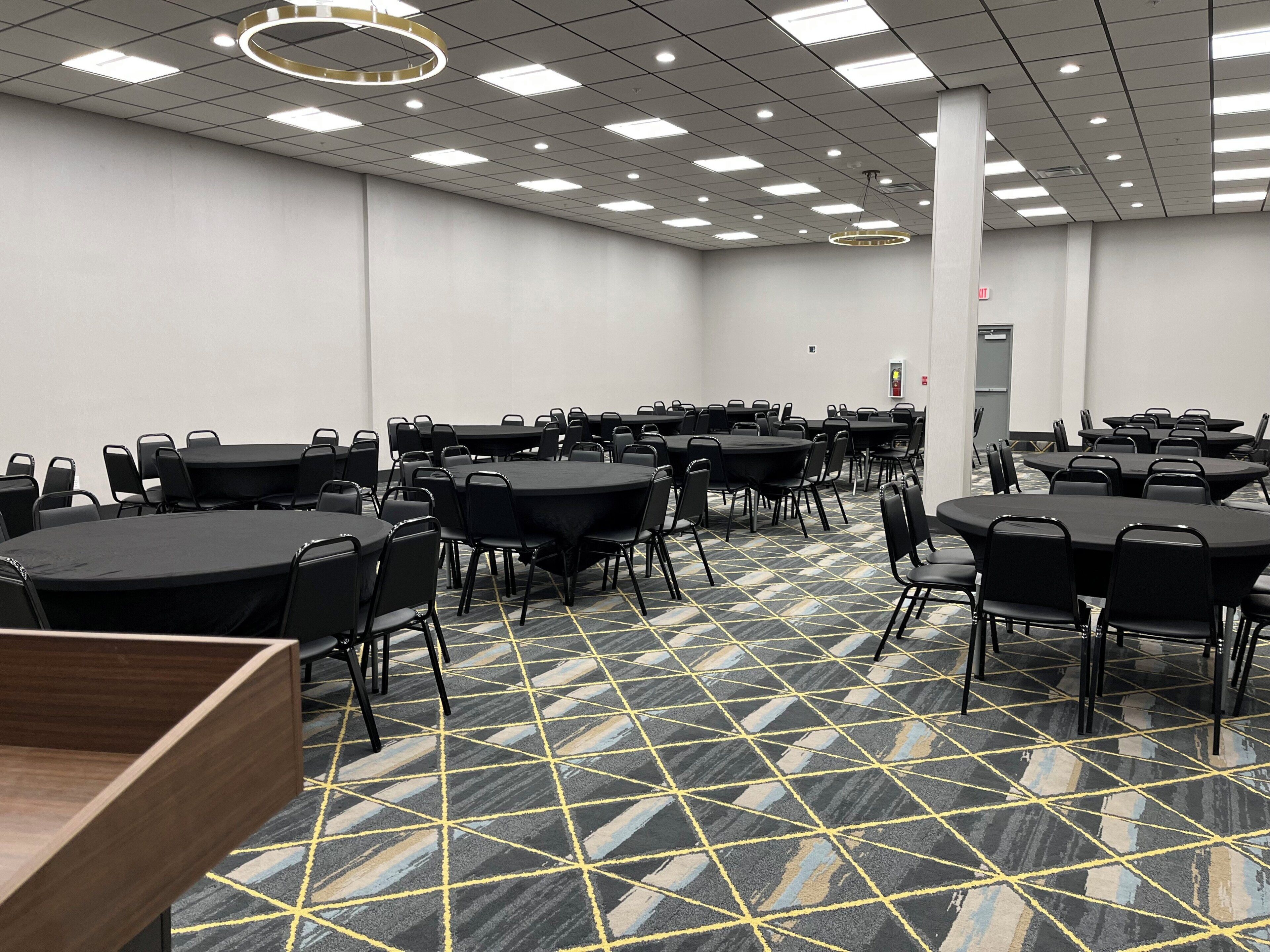 A conference room with multiple tables and chairs, a patterned carpet, and a ceiling with recessed lighting.