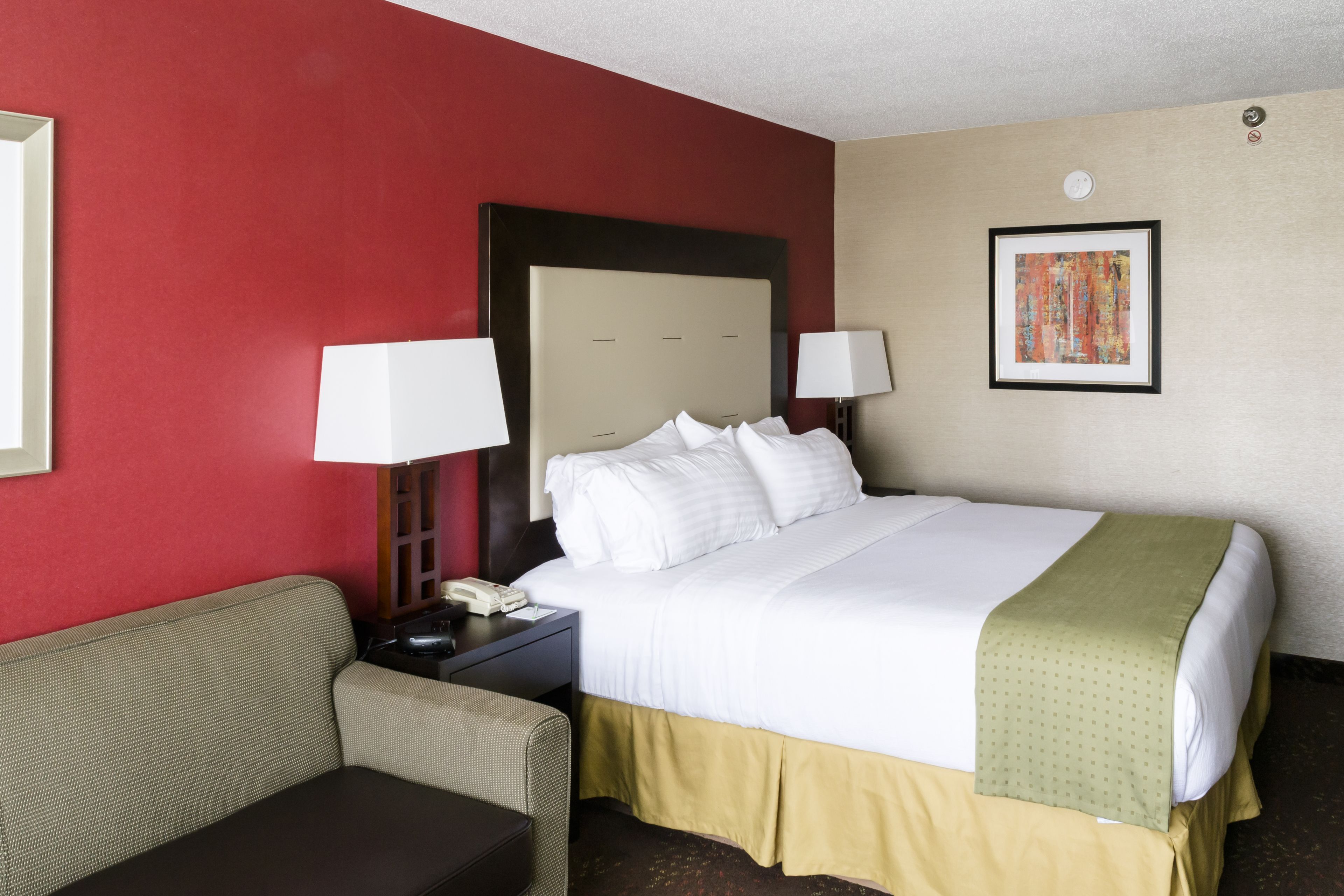 A hotel room with a bed, a nightstand, a lamp, a sofa, and a framed picture on the wall.