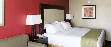A hotel room with a bed, a nightstand, a lamp, a sofa, and a framed picture on the wall.