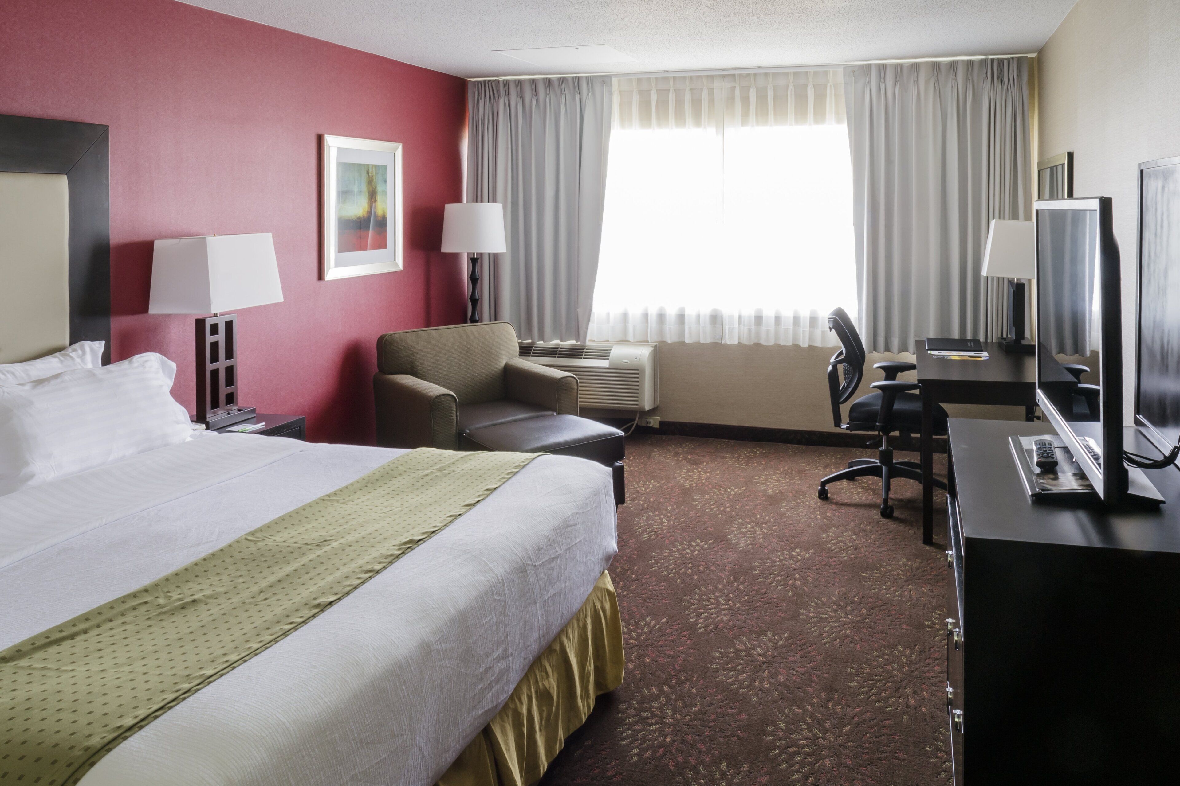 Habitación de hotel con una cama grande, un escritorio con computadora, una silla y un televisor.