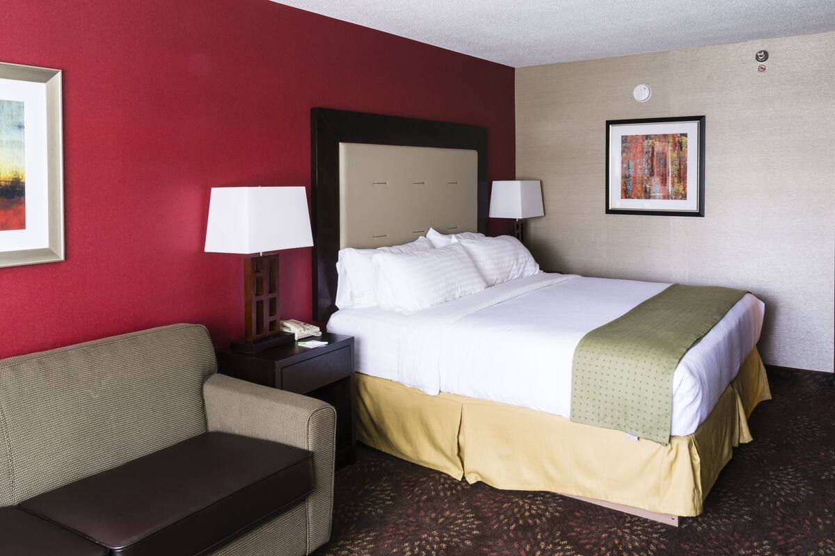 Una habitación de hotel con cama, mesita de noche, lámpara, sofá y un cuadro en la pared.