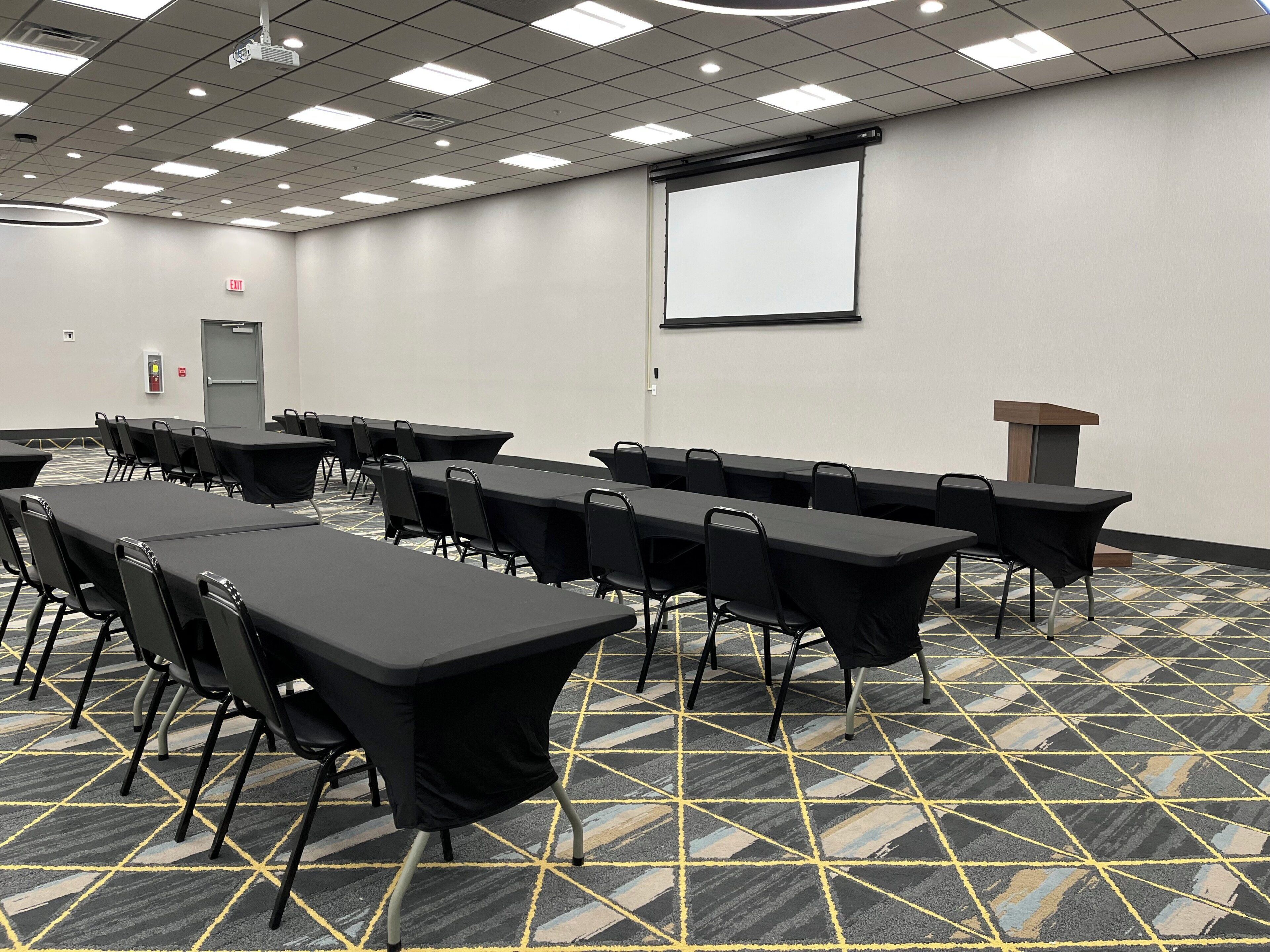 A conference room with tables, chairs, a projector screen, and a podium.