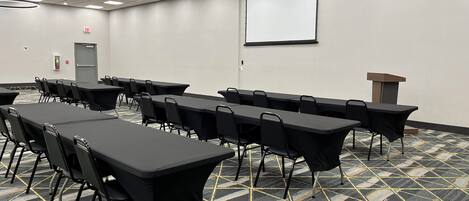 A conference room with tables, chairs, a projector screen, and a podium.