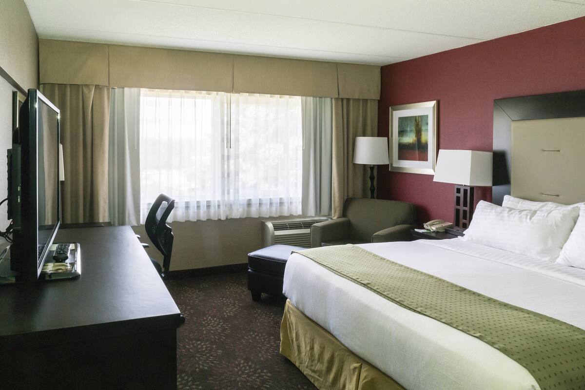 Habitación de hotel con una cama grande, un escritorio con computadora y teléfono, una silla y una ventana con cortinas.