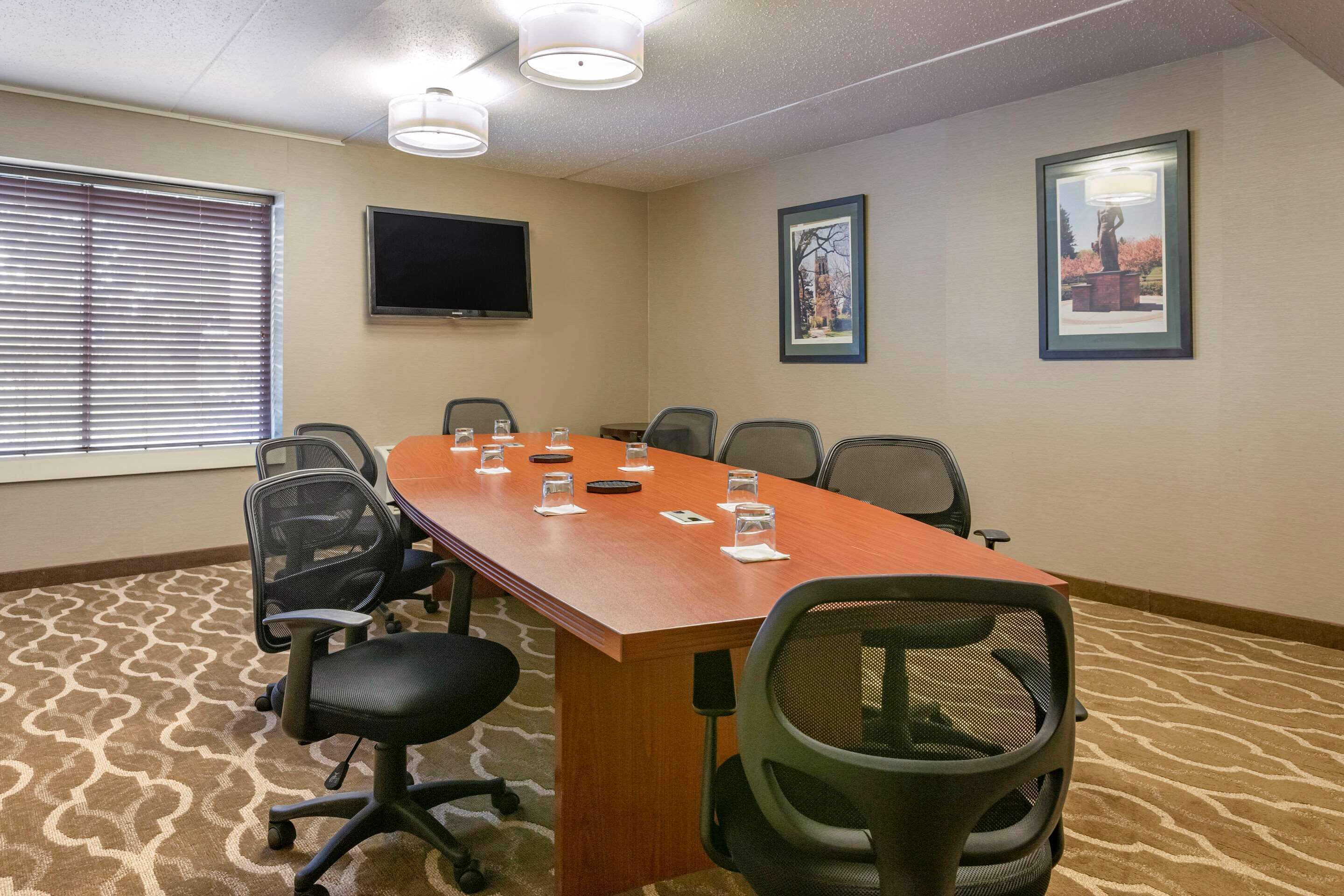 A conference room with a long table, chairs, a flat-screen TV, framed pictures, and patterned carpet.