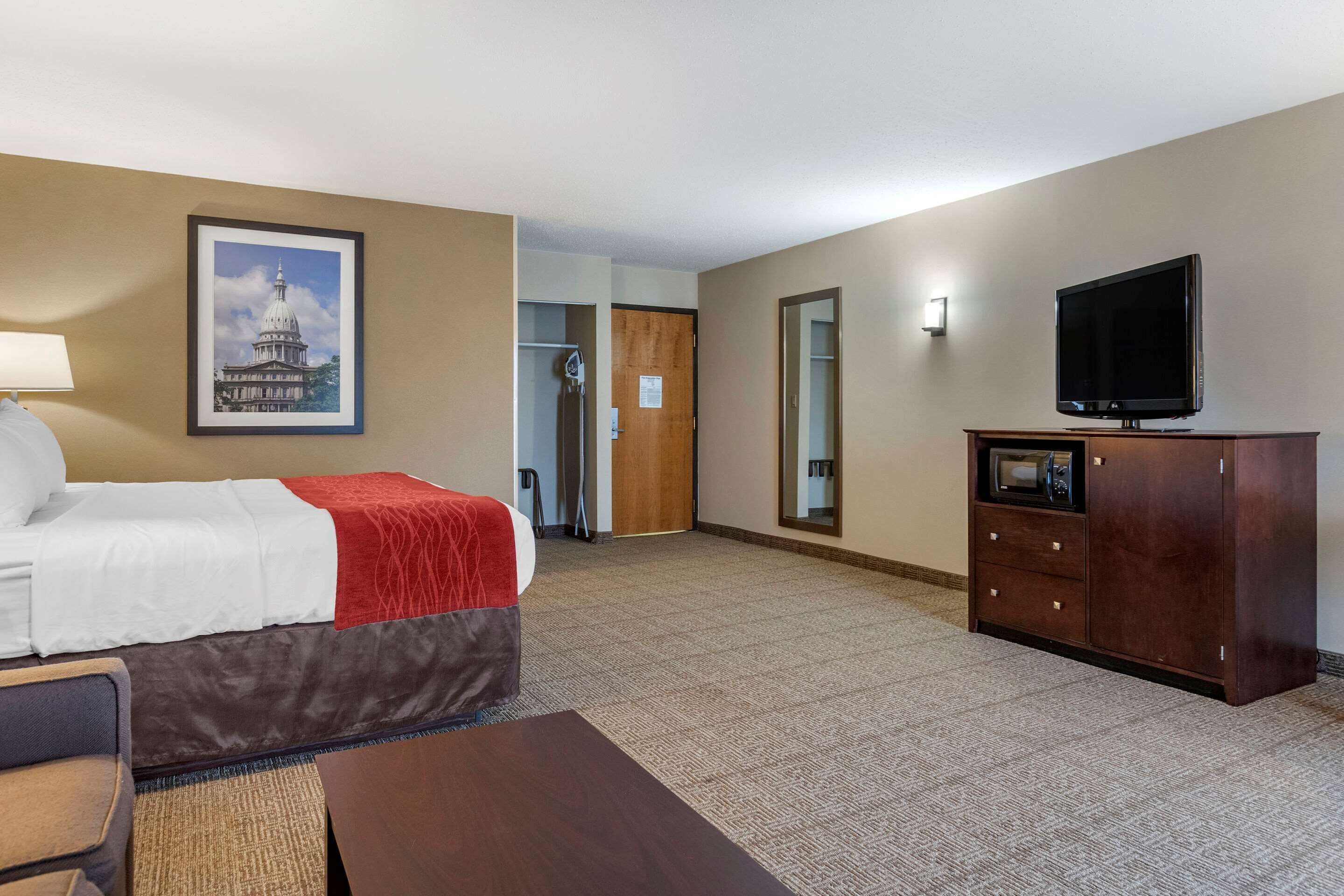 Una habitación de hotel con una cama, un televisor, un armario de madera y un cuadro enmarcado en la pared.