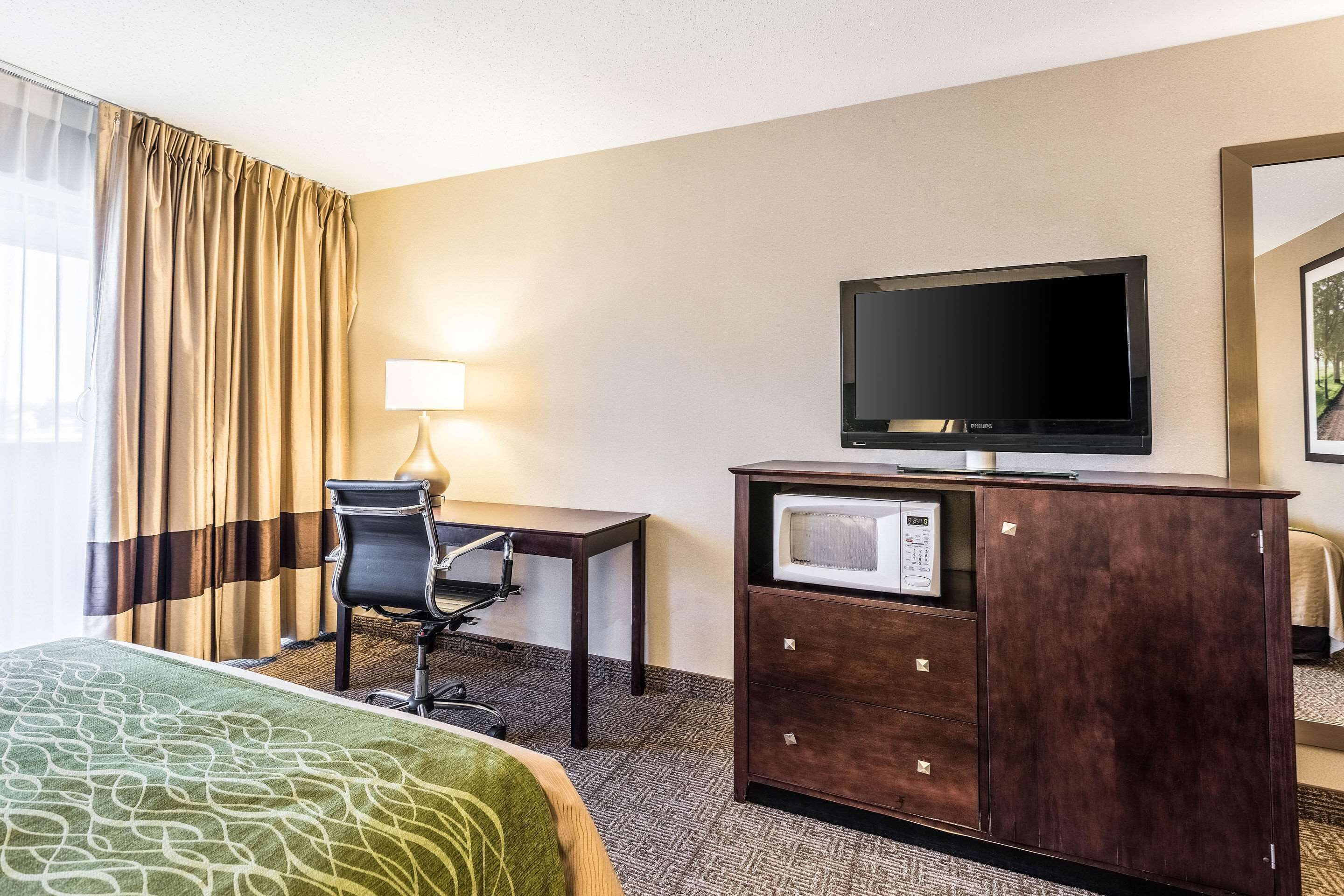 A hotel room with a bed, a desk, a television, a microwave, and a chair.