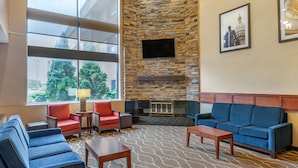 A lobby with a stone fireplace, blue sofas, and a television mounted on the wall. - Comfort Inn Lansing West (Lansing)