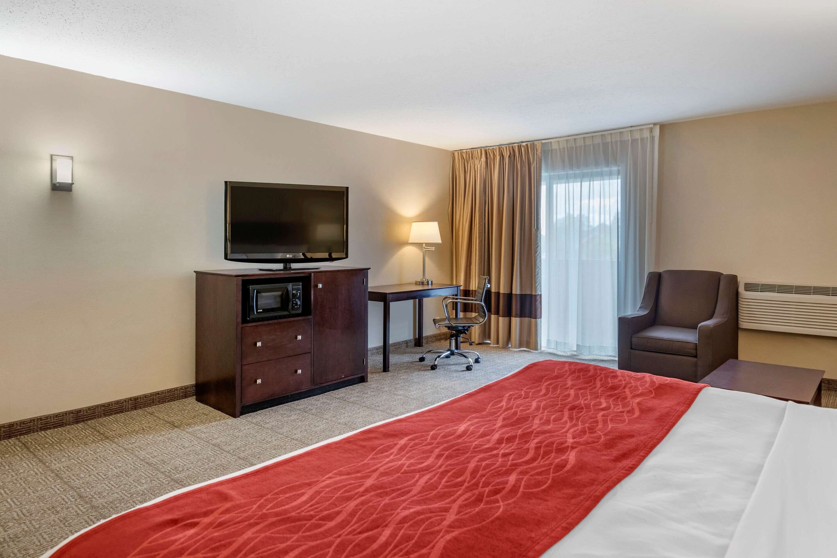 Ein Hotelzimmer mit einem großen Bett, einem Schreibtisch mit Stuhl, einem Fernseher, einer Mikrowelle und einem Sessel.