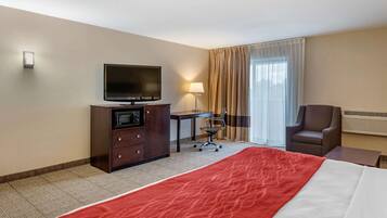 Ein Hotelzimmer mit einem großen Bett, einem Schreibtisch mit Stuhl, einem Fernseher, einer Mikrowelle und einem Sessel.