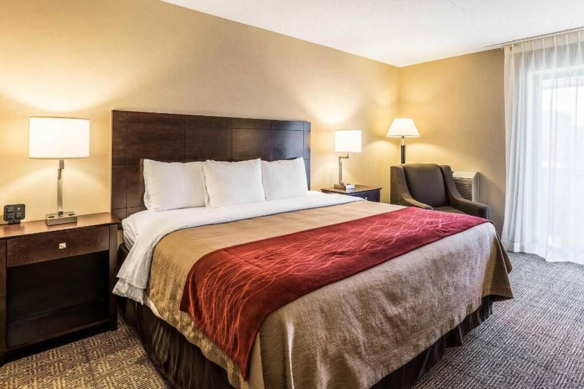 A hotel room with a large bed, two bedside tables with lamps, a chair, and a window with curtains.