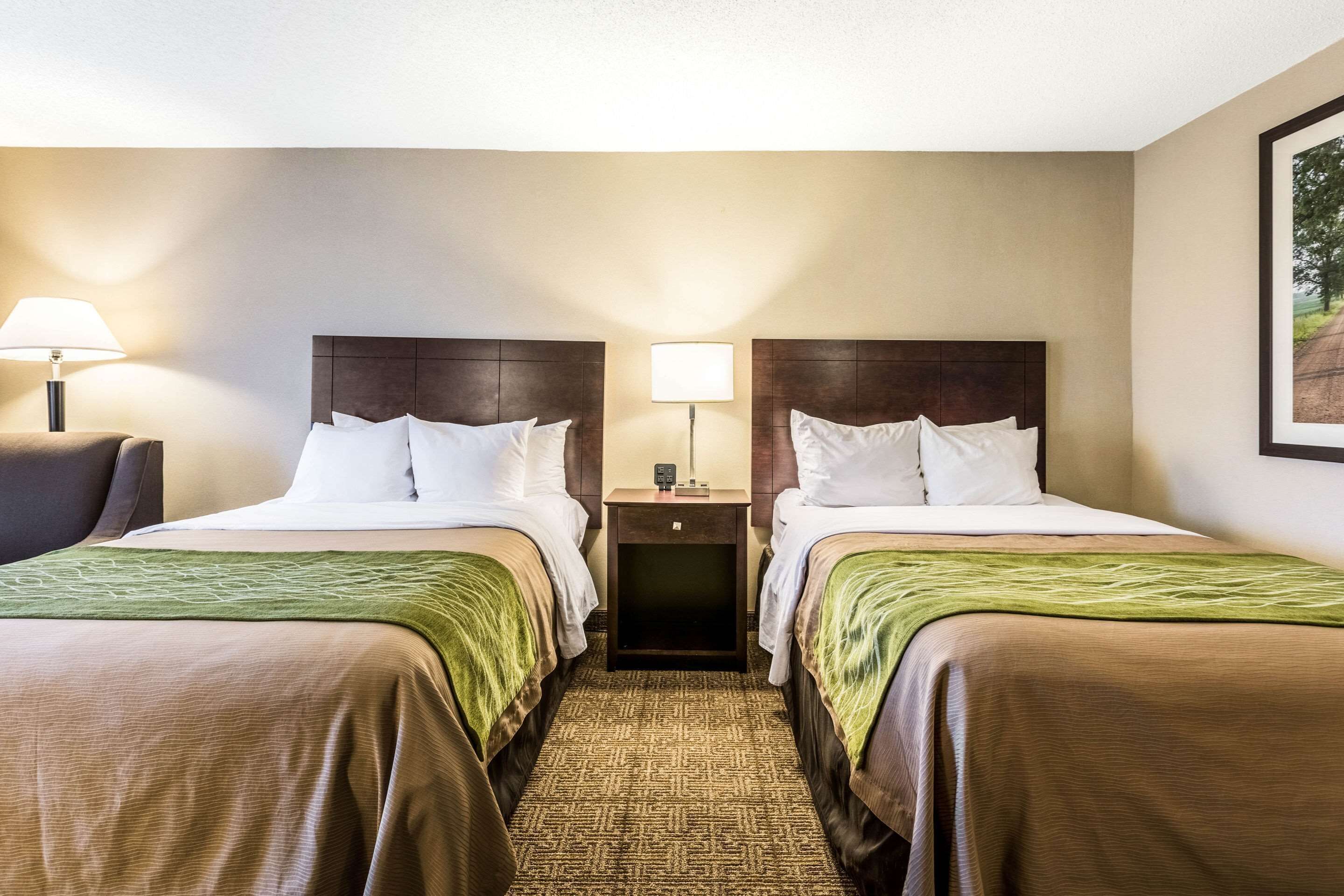 Habitación de hotel con dos camas, una mesita de noche y una lámpara entre ellas.