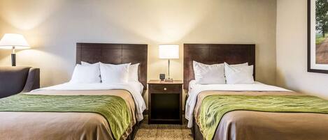 Habitación de hotel con dos camas, una mesita de noche y una lámpara entre ellas.