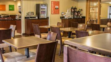 A restaurant with wooden tables and chairs, a coffee machine, and a refrigerator.