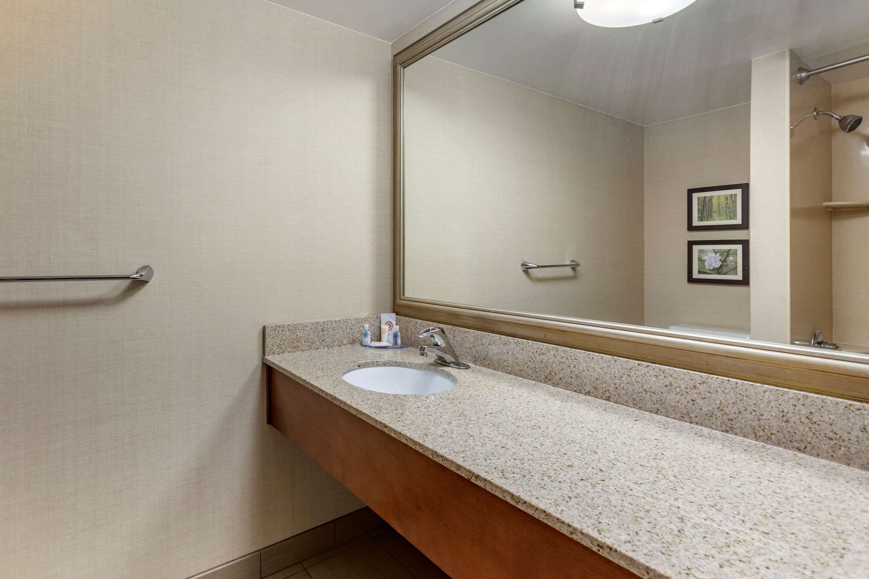 Ein Badezimmer mit Waschbecken, Spiegel, Handtuchhalter und gerahmten Bildern an der Wand.
