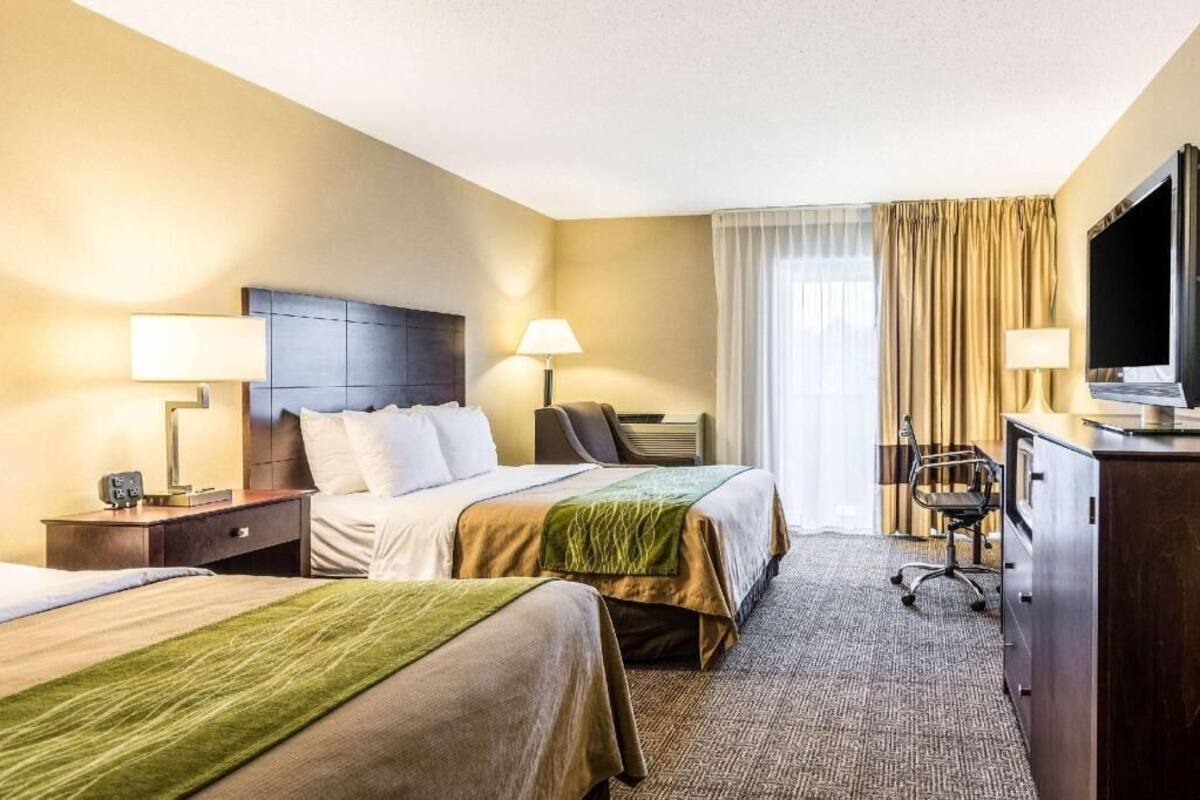 A hotel room with two beds, a desk, a chair, a television, and a window with curtains.