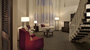 Een ruime woonkamer met een rode fauteuil, een witte bank en een salontafel. Een trap met witte spijlen leidt naar de bovenverdieping.