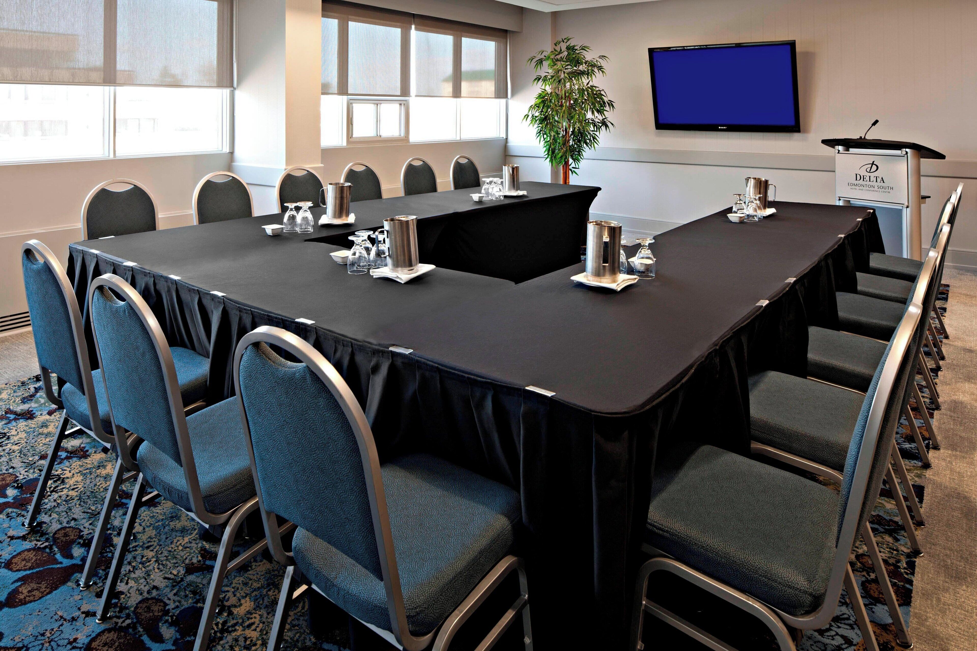 A conference room with a long table, chairs, a podium, and a television screen.