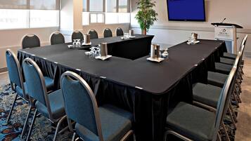 A conference room with a long table, chairs, a podium, and a television screen.
