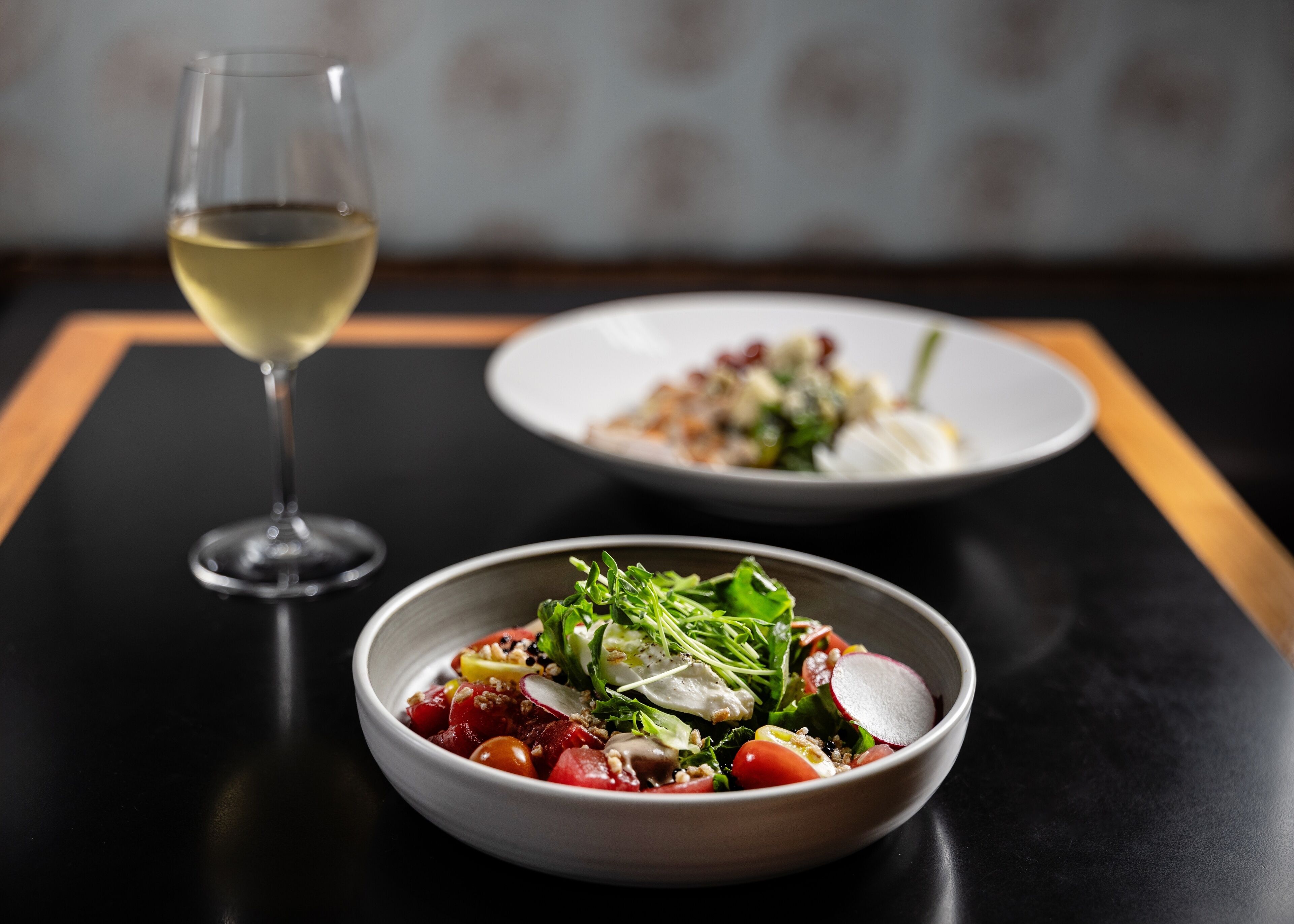 A dining table with two plates of food and a glass of white wine.