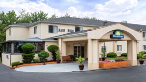 A Days Inn with a beige exterior, a covered entrance, and a small patio area with a bench and potted plants. - Days Inn by Wyndham Runnemede Philadelphia Area (Runnemede)