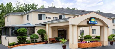 A Days Inn with a beige exterior, a covered entrance, and a small patio area with a bench and potted plants.