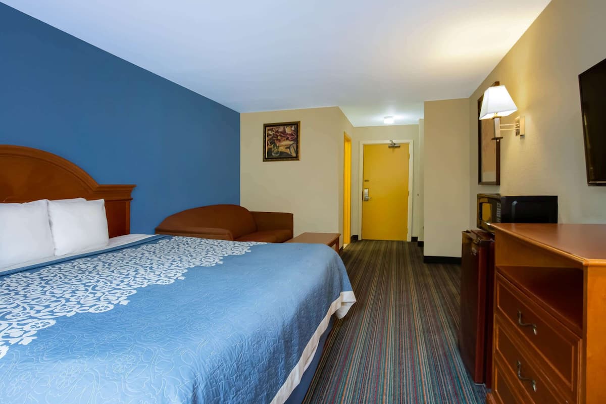 A hotel room with a large bed, a wooden dresser, a desk, and a chair.