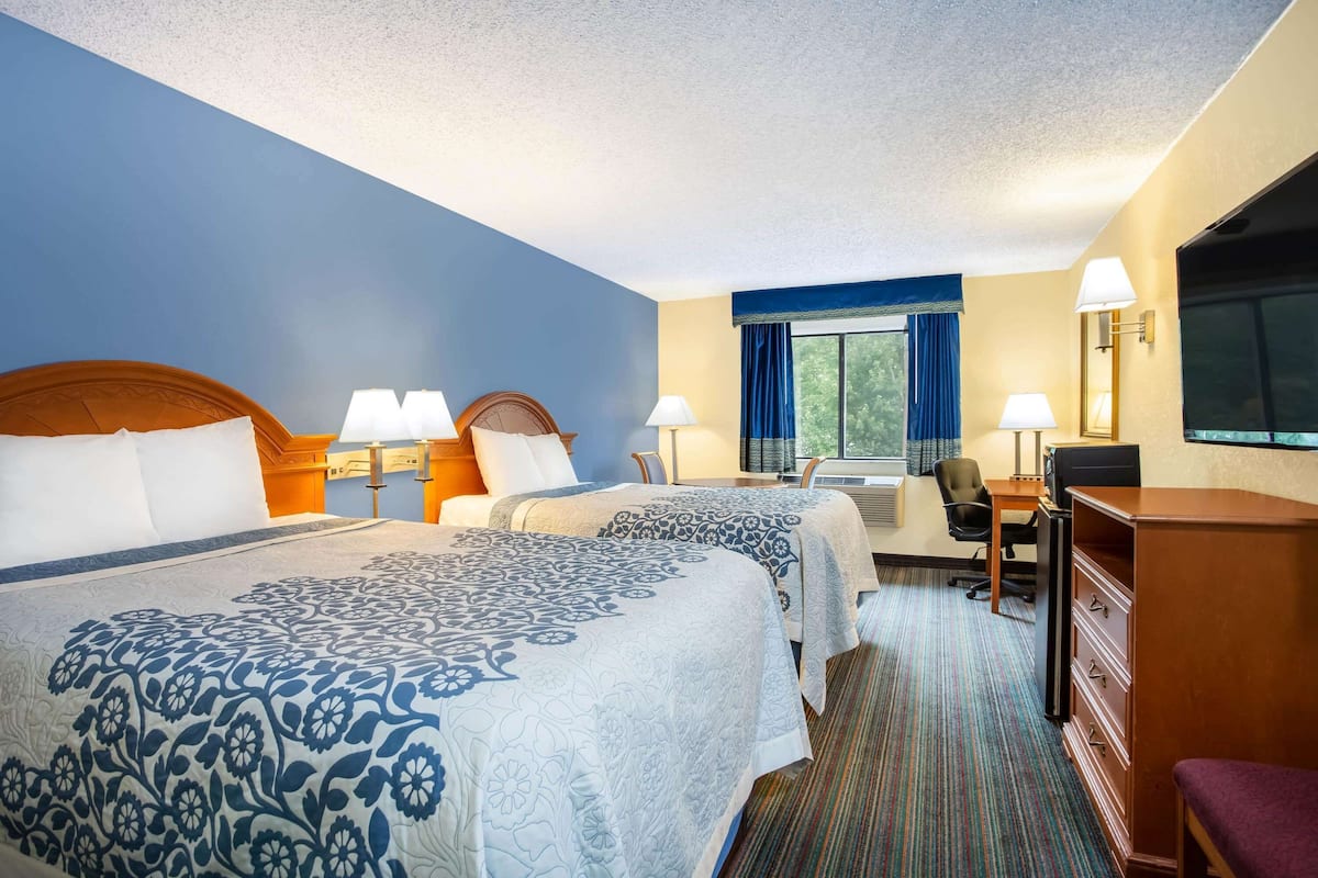 A hotel room with two beds, a desk, a chair, a TV, and a dresser.