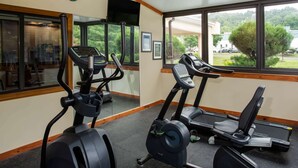 A gym with treadmills and an elliptical machine, large windows with a view of greenery and buildings, and a clock on the wall. - Days Inn by Wyndham Runnemede Philadelphia Area (Runnemede)
