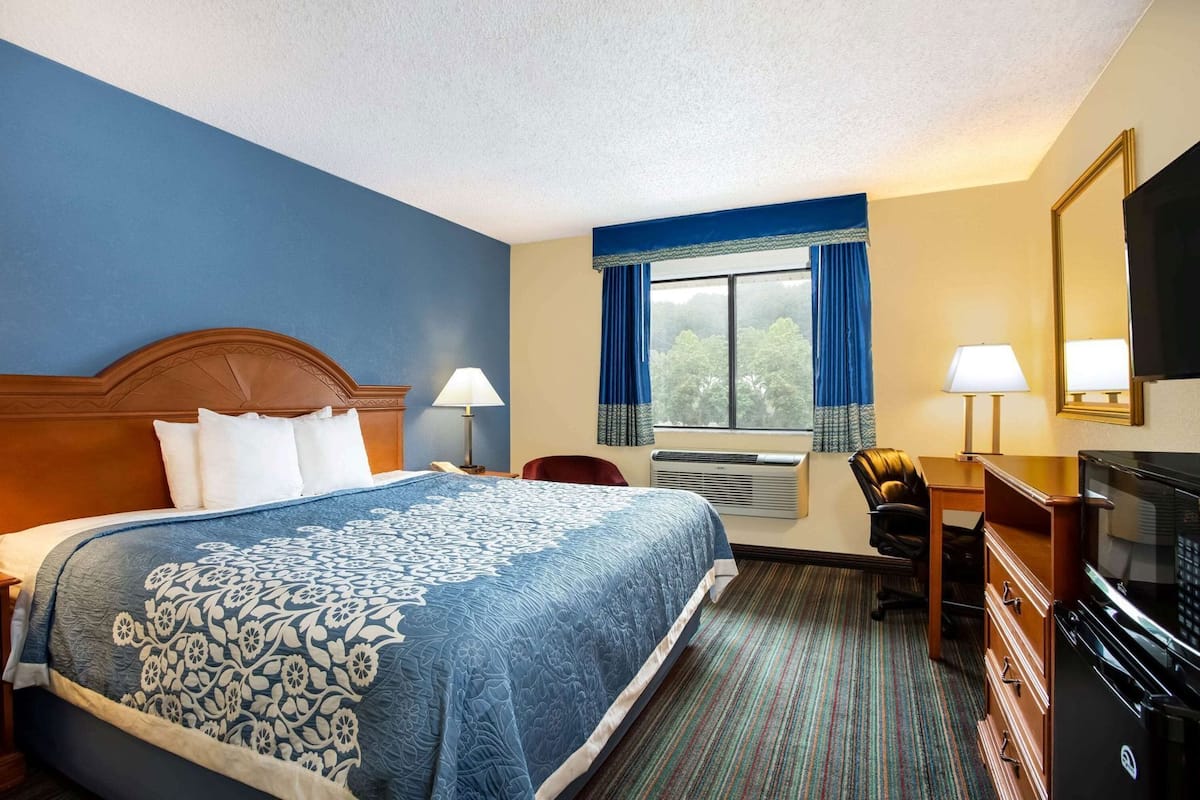 A hotel room with a large bed, a desk, a chair, a television, and a window with curtains.