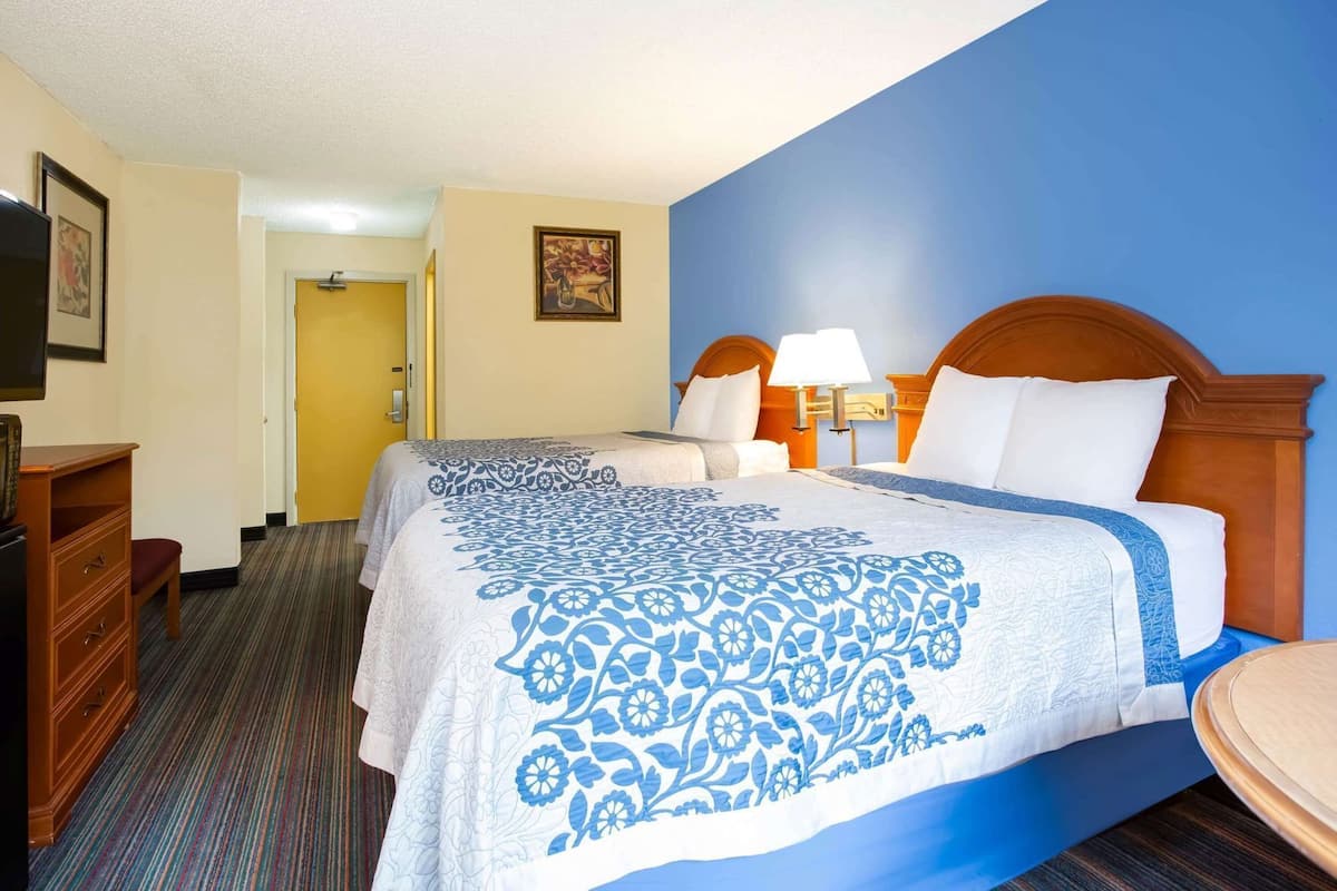A hotel room with a bed, bedside lamps, a dresser, and a door leading to another room.