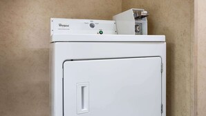A white Whirlpool washer and dryer stacked in a corner with beige walls. - Days Inn by Wyndham Runnemede Philadelphia Area (Runnemede)