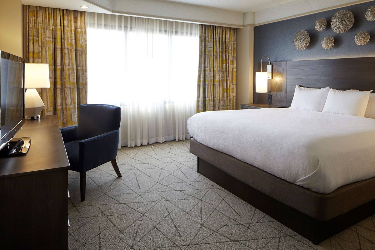Une chambre d’hôtel avec un grand lit, un bureau avec une lampe, une chaise et un téléviseur.