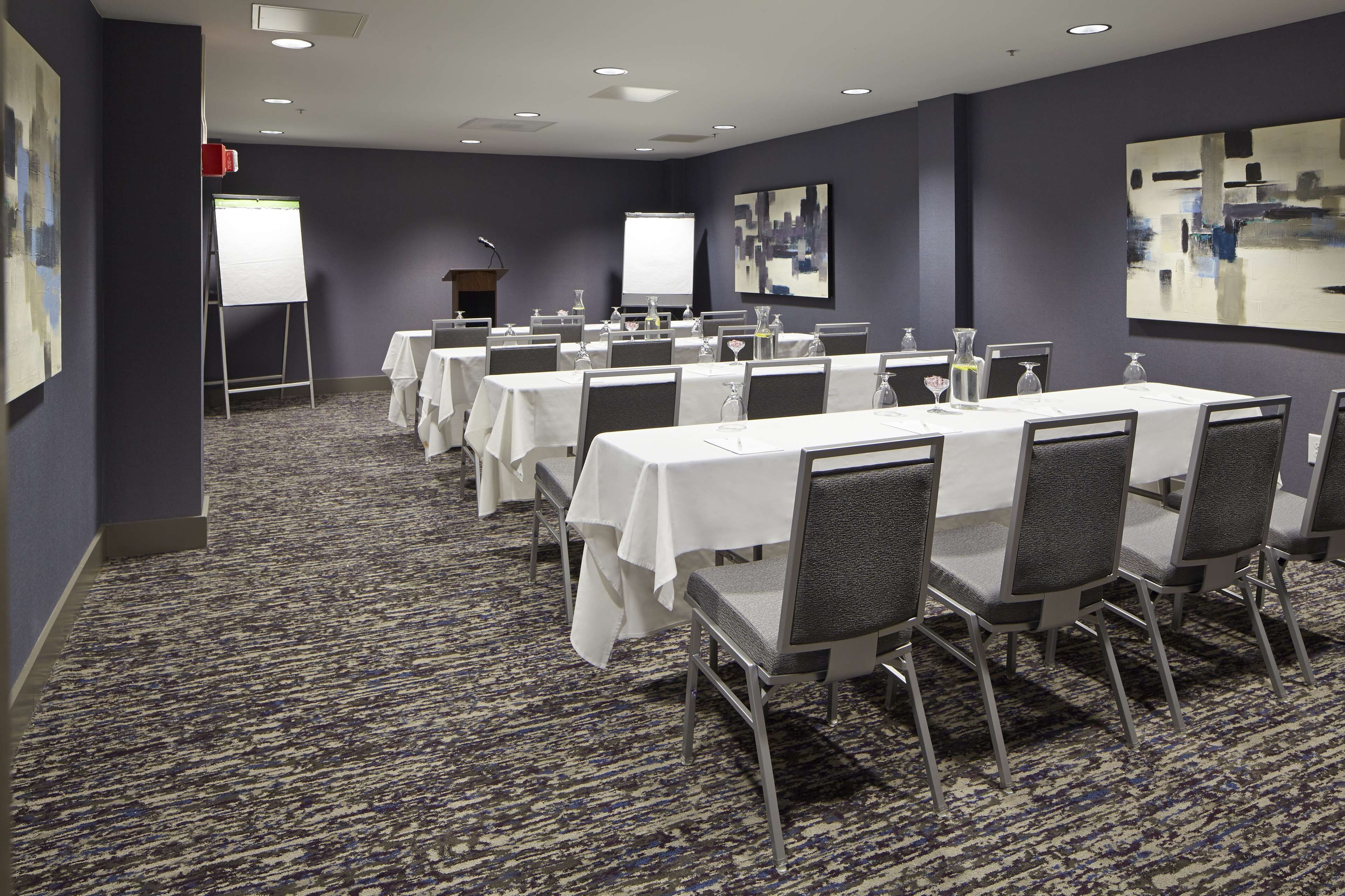 A conference room with multiple tables and chairs, a whiteboard, a projector screen, and a podium.
