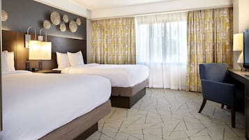 A hotel room with two beds, a desk, a chair, and a large window with curtains.