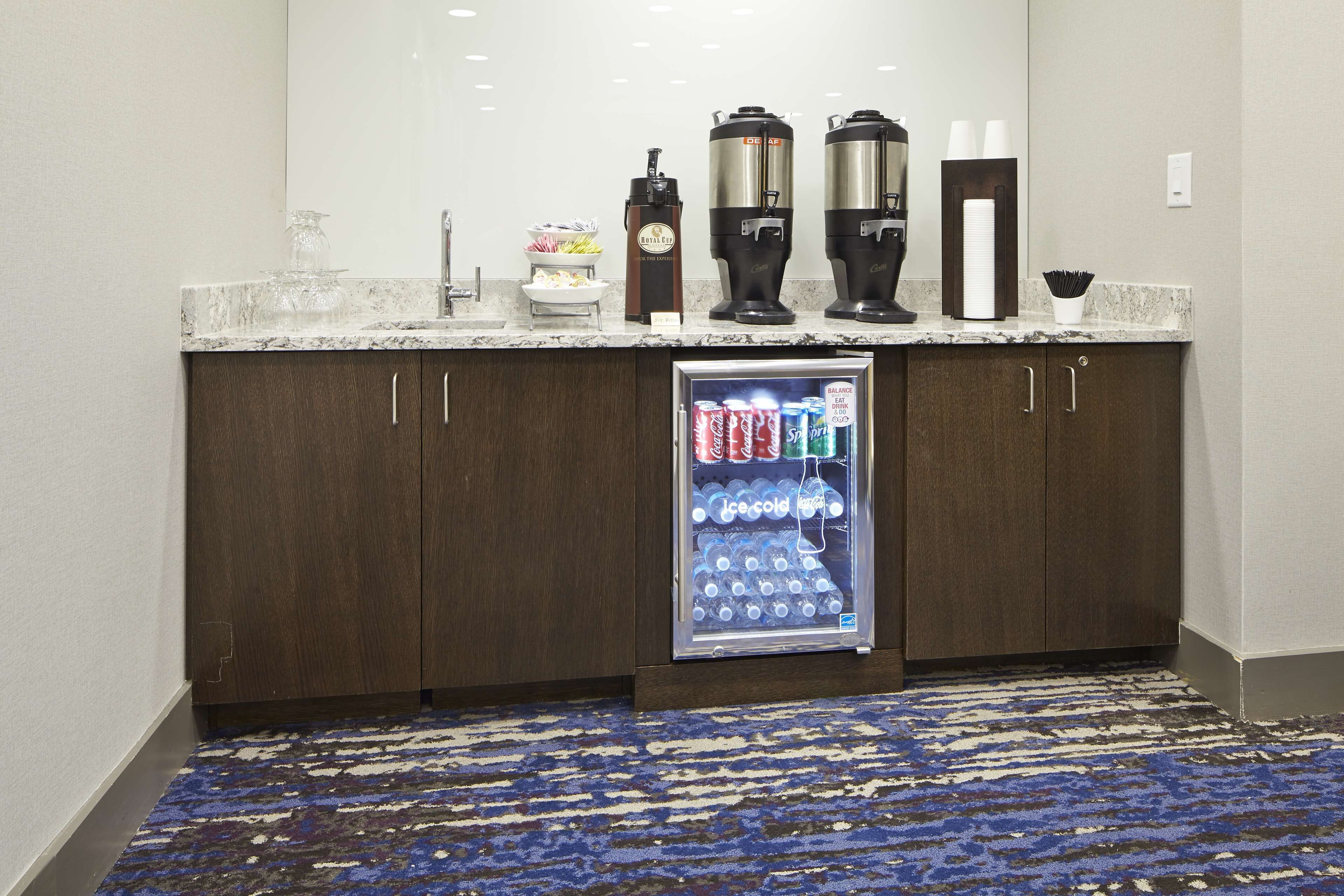 A minibar with a refrigerator stocked with beverages, a coffee maker, and a tea dispenser.