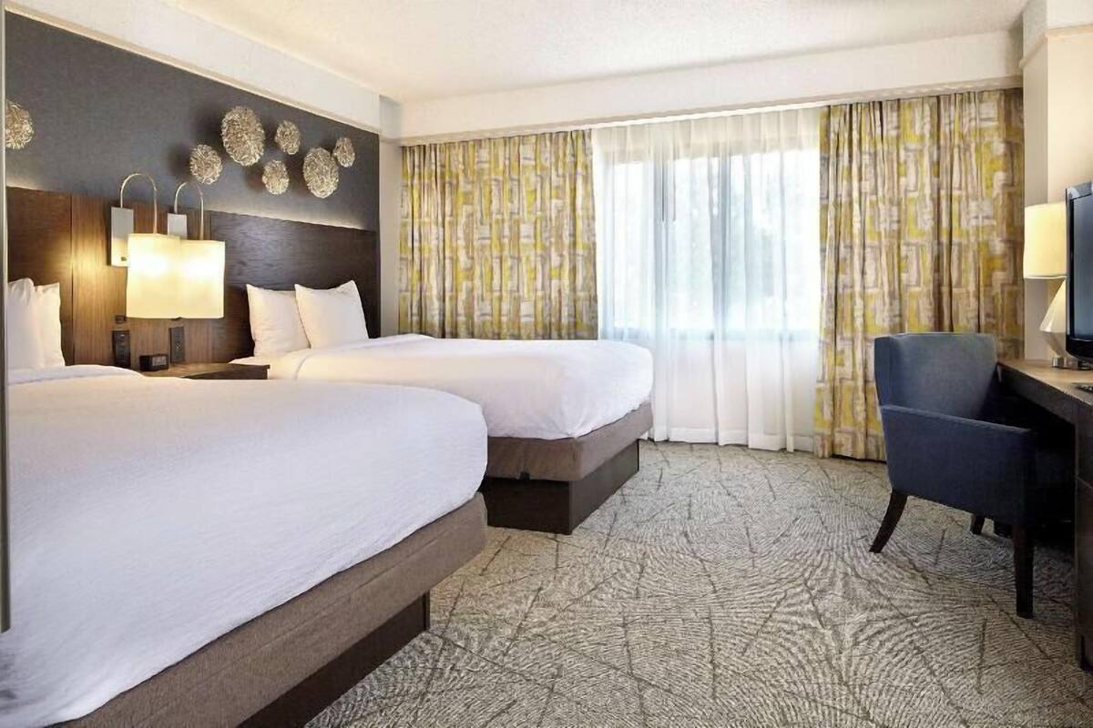 Une chambre d’hôtel avec deux lits, un bureau, une chaise et un téléviseur.